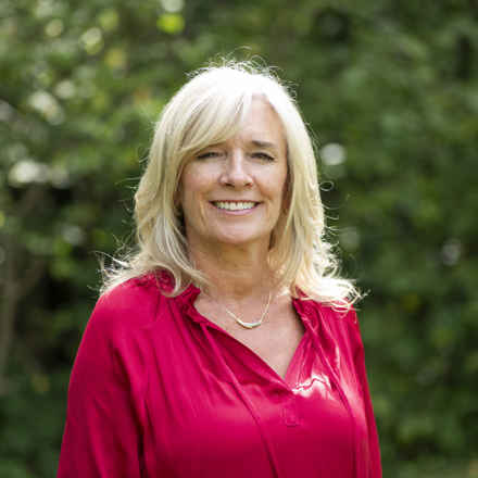 Headshot of Suzanne a white woman with long blonde hair wearing a bright pink blouse