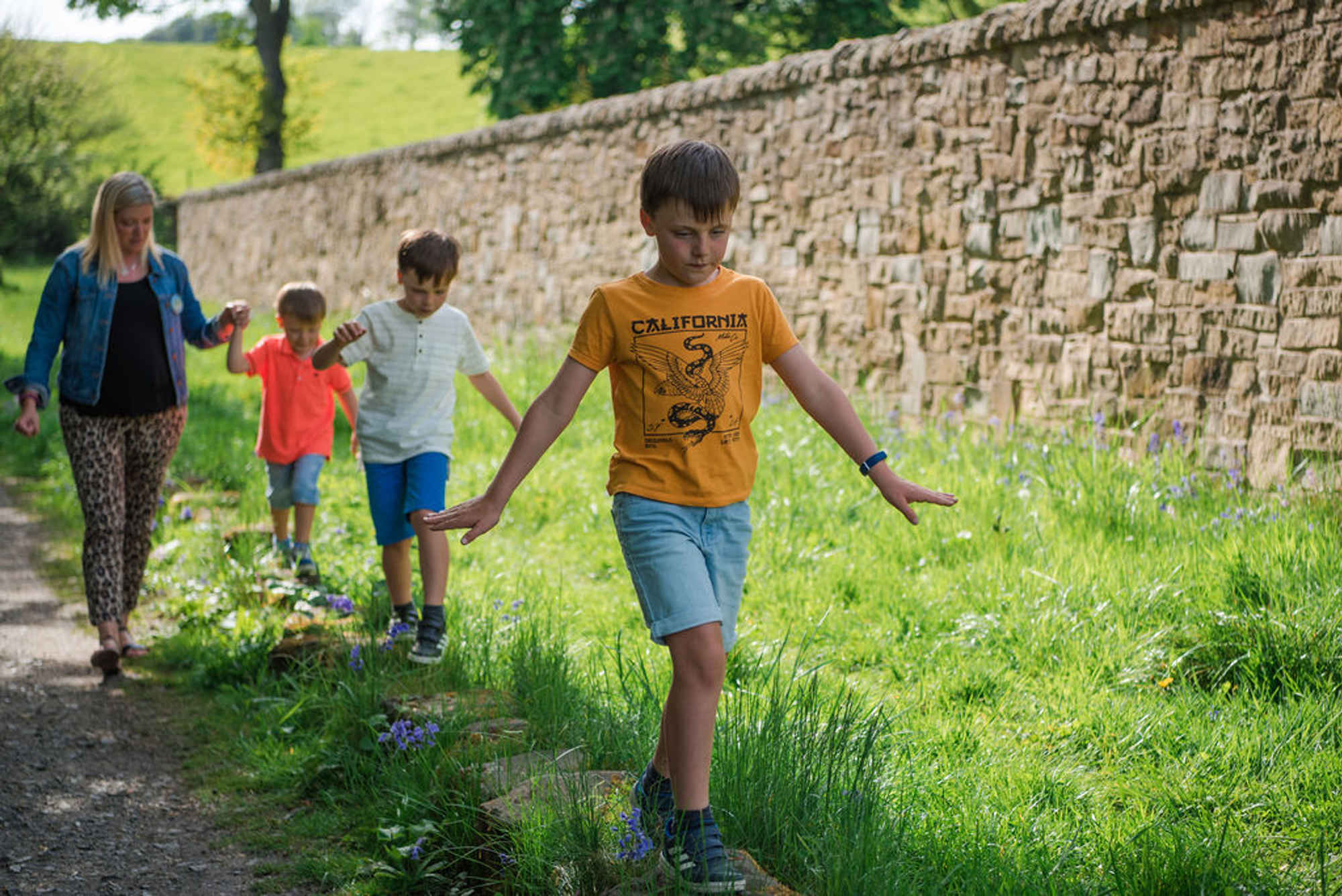 Young boys walking along stones beside a track in summer, the last holding hands with their mother
